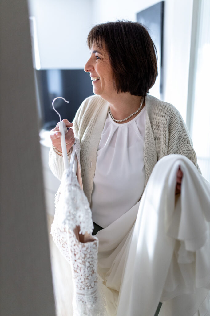 Die Mutter der Braut steht im Türrahmen und hält das Brautkleid in den Händen.