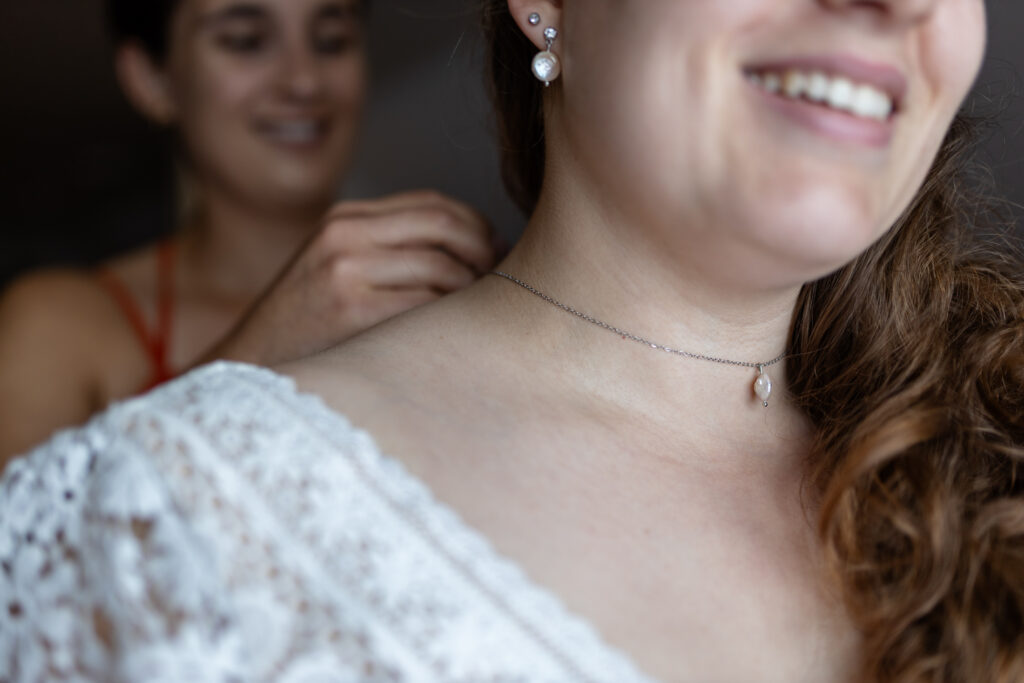 Nahaufnahme der Halskette der Braut, während die Trauzeugin ihr die Kette gerade anlegt.