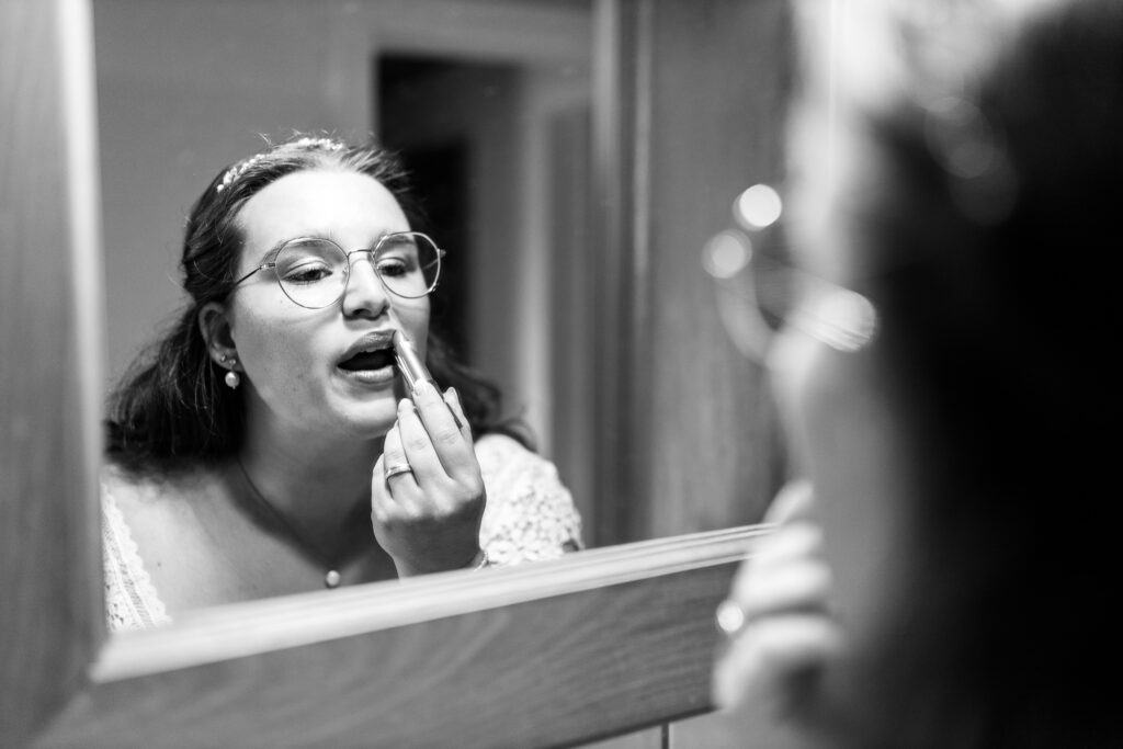Getting ready Braut: die Braut steht im Badezimmer vor dem Spiegel und zieht sich den Lippenstift nach. Schwarz-weiss Foto.