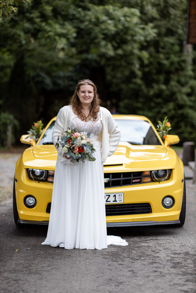 Portrait von der Braut, wie sie vor ihrem Hochzeits-Auto (einem gelben Ford Mustang) posiert.