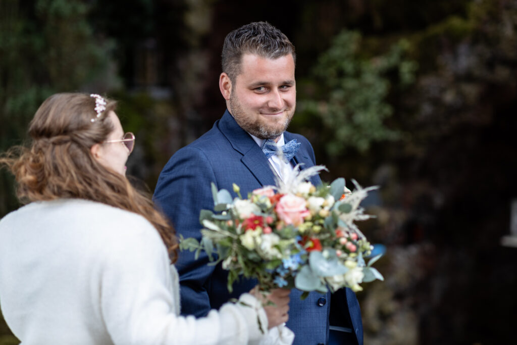 Der Bräutigam dreht sich gerade für den First Look um und sieht aus den Augenwinkeln seine Frau zum ersten Mal im Hochzeitskleid. Die Braut ist auf dem Foto nur von hinten zu sehen.