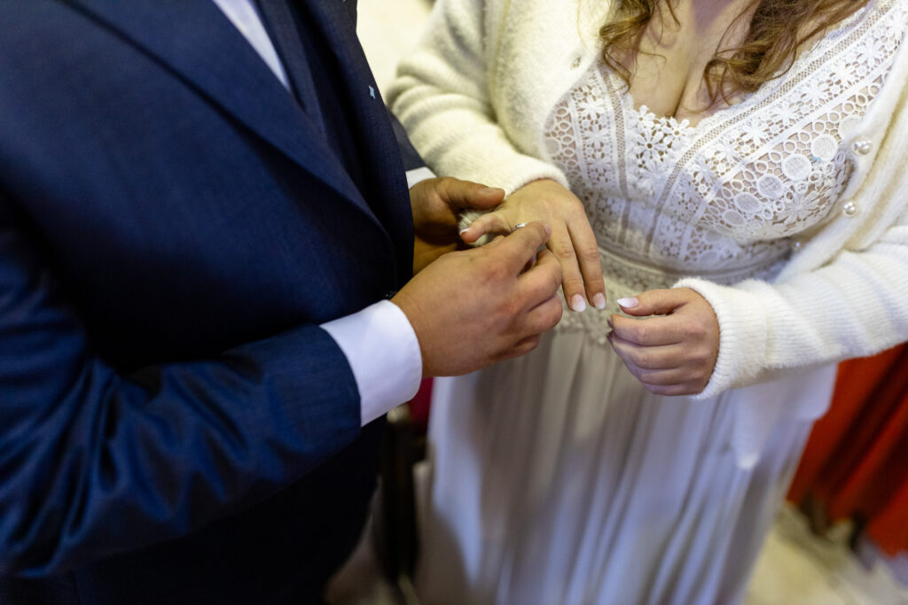 Nahaufnahme des Ringtauschs bei der Hochzeits-Zeremonie in der kirche. Man sieht nur die Arme und Hände des Paars, während er ihr gerade den Ring ansteckt.