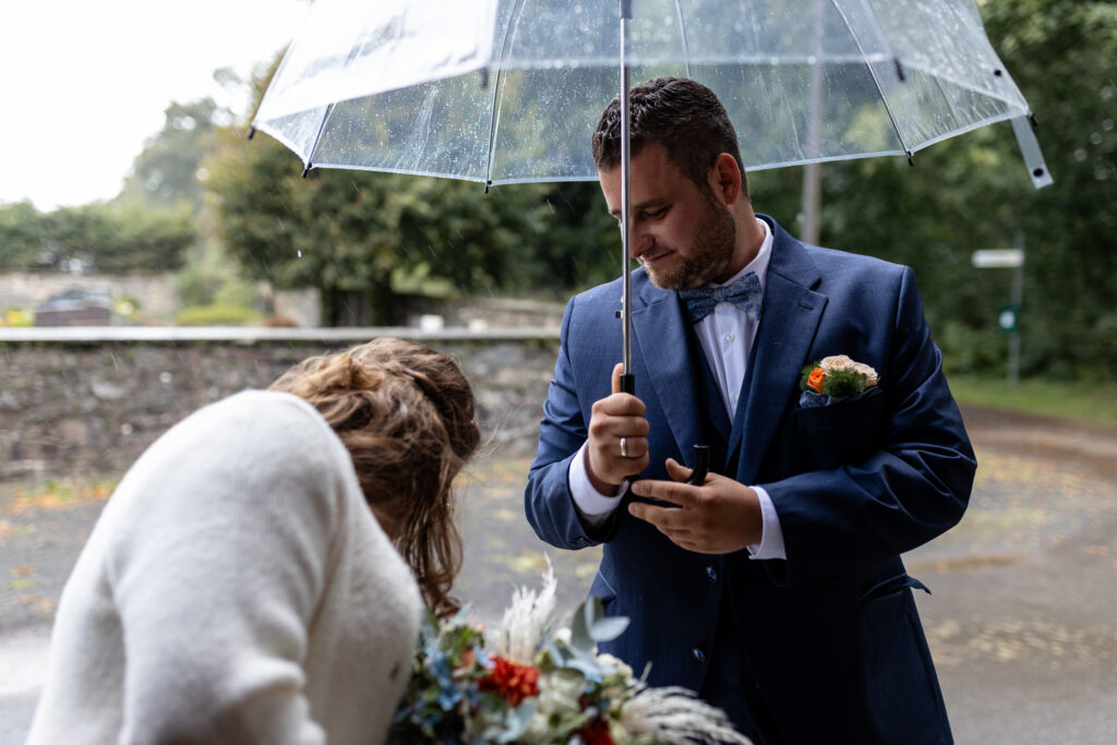 Nach der kirchlichen Hochzeit steht das Paar vor der Kirche im Regen. Er halät ihr den Schirm.