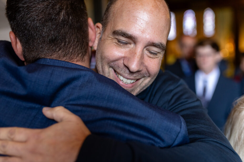 Nahaufnahme: Ein Freund gratuliert dem Bräutigam. Man sieht sein Gesicht und den Rücken des Bräutigams.