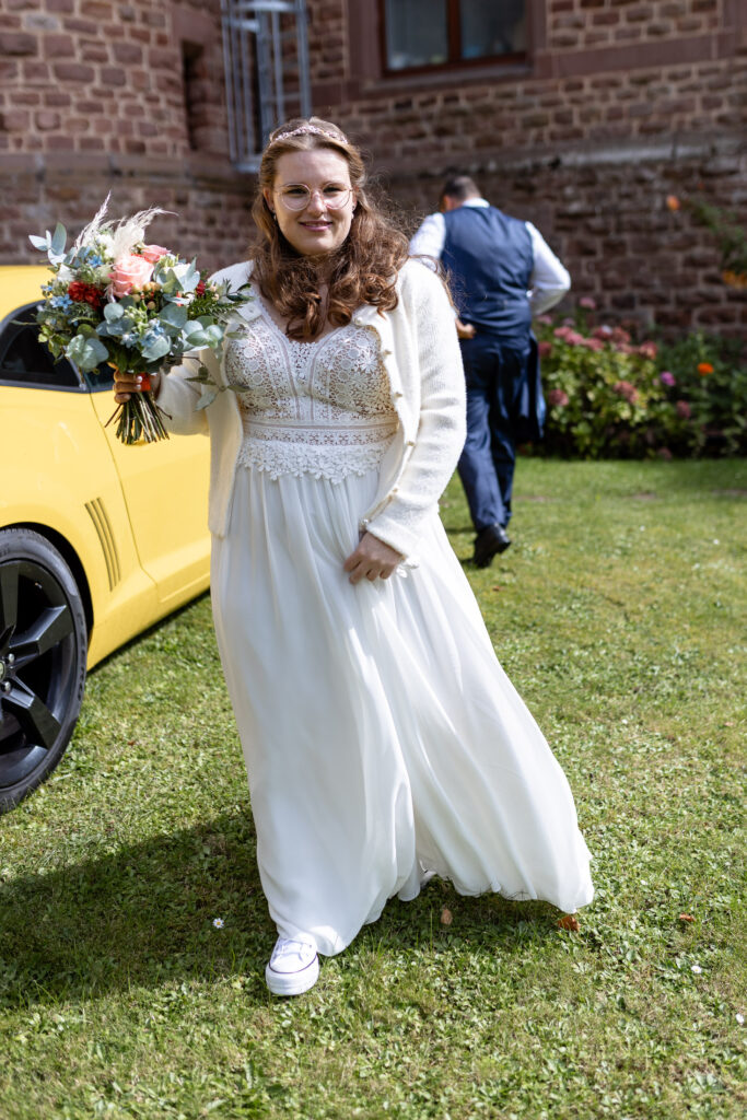 Die Braut kommt auf den Fotografen zu, nachdem sie aus dem gelben Fords Mustang (Sportwagen) ausgestiegen ist. Sie ist auf dem Weg zum Eingang des Schloss.