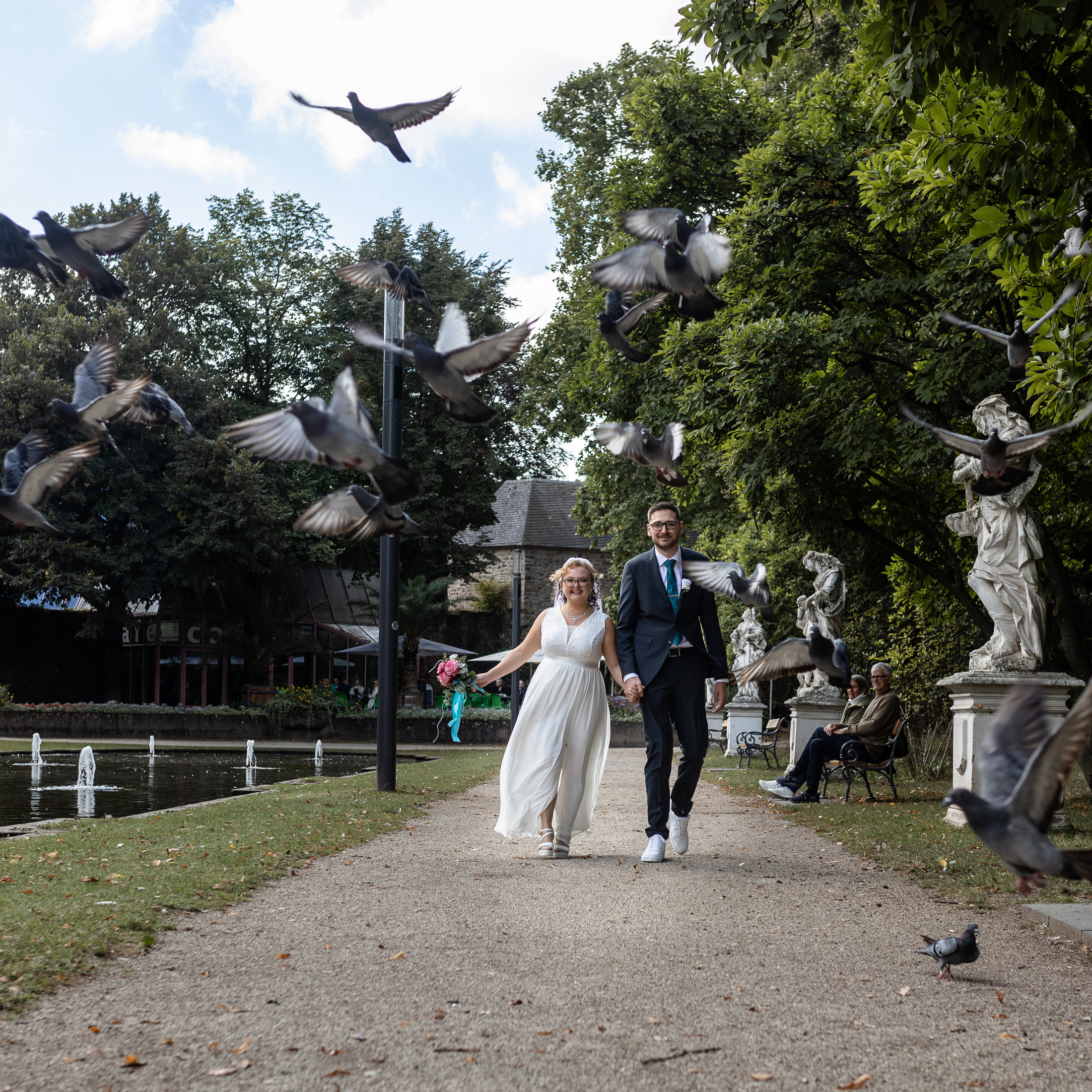 Brautpaar spaziert durch den Trierer Palastgarten, Tauben fliegen herum