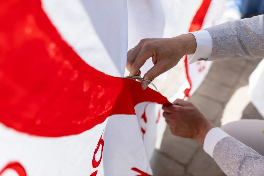 Hochzeitsfotograf Bernkastel Trier - Nahaufnahme: Man sieht ein Bettlaken, welches von den Händen des Bräutigam und einer Nagelschere durchgeschnitten wird.