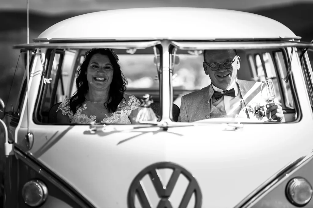 Hochzeitsfotograf Bernkastel Trier - Stimmungsvolle schwarz-weiss Aufnahme des Brautpaars, das im Volkswagen T1 Bulli sitzt und in die Kamera lächelt.
