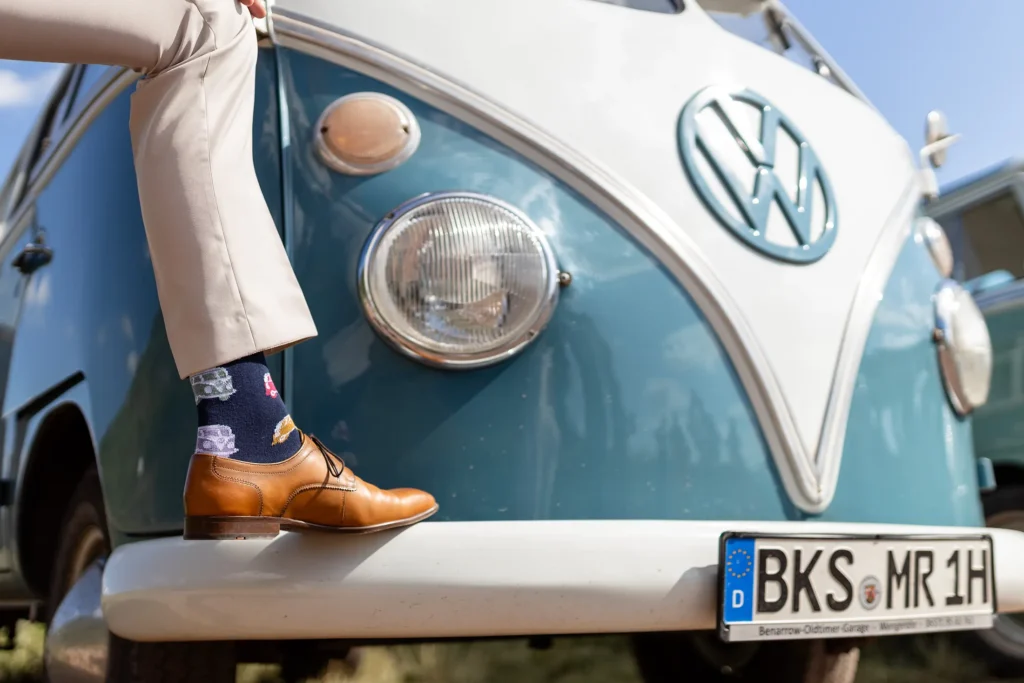 Hochzeitsfotograf Bernkastel Trier - Detailaufnahme der Socken des Bräutigams, auf denen T1 Bullis abgebildet sind. Man sieht nur das Bein des Bräutigams, was auf der Stoßstange eines T1 Busses steht