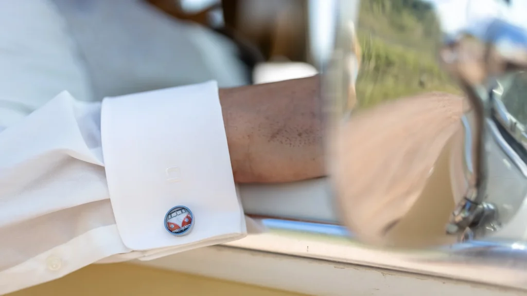 Hochzeitsfotograf Bernkastel Trier - Detailaufnahme der Manschetten Knöpfe des Bräutigams auf denen ein VW T1 Bulli zu sehen ist. Man sieht nur den aus dem T1 Bus herausgestreckten Arm und erkennt noch gerade so den Spiegel des T1 Bus, in dem der Bräutigam sitzt.