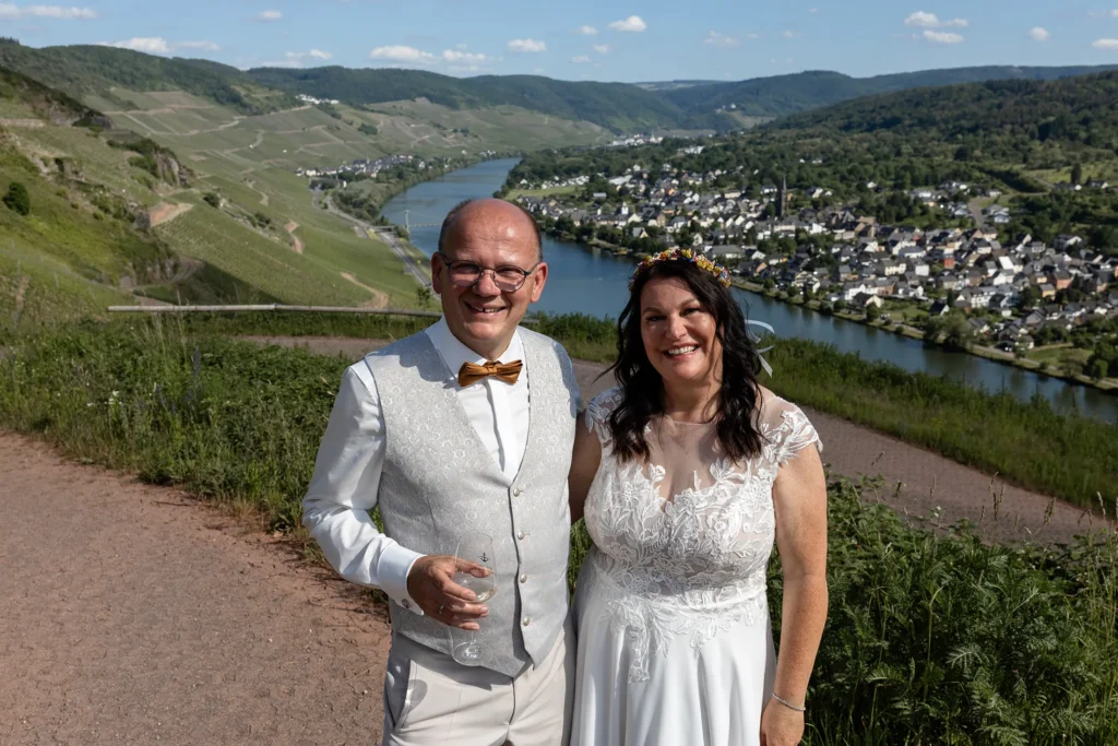 Hochzeitsfotograf Bernkastel Trier - Brautpaar posiert für das Foto in den Weinbergen von Bernkastel und im Hintergrund sieht man das Tal, die Mosel und Bernkastel.