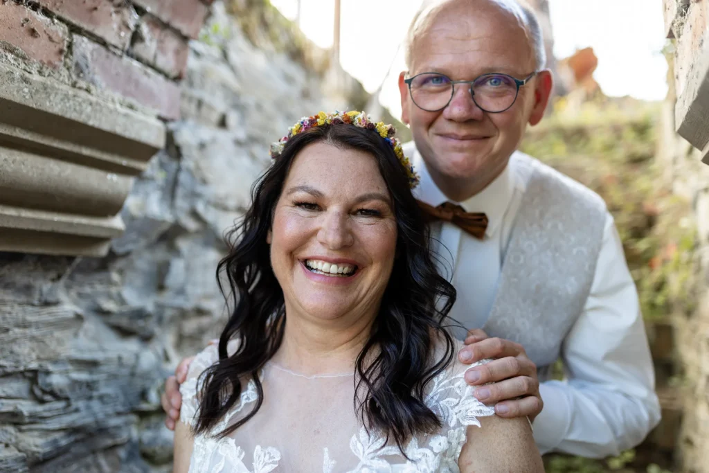 Hochzeitsfotograf Bernkastel Trier - Brautpaar-Shooting: Bräutigam steht hinter der Braut und hält sie an den schultern. Beide lächeln in die Kamera.