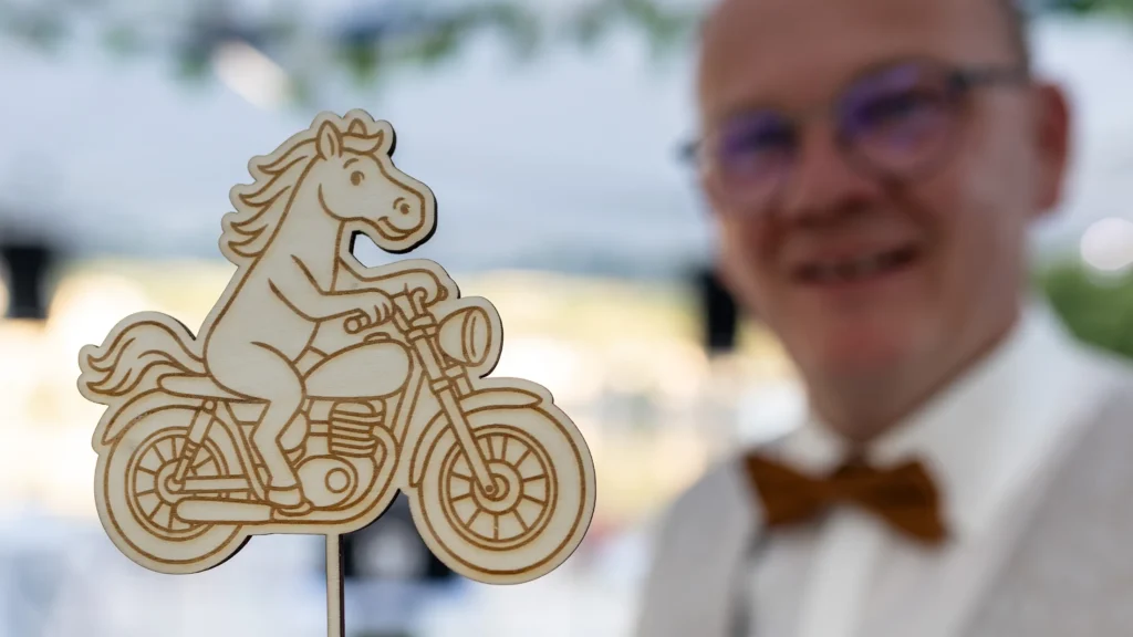 Hochzeitsfotograf Bernkastel Trier - Detailaufnahme eines Motorrad fahrenden Pferds, was als Aufsatz auf die Hochzeitstorte gesteckt wurde. Im Hintergrund ist unscharf der Bräutigam zu sehen.