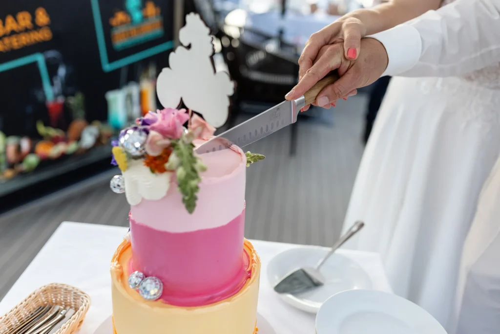 Hochzeitsfotograf Bernkastel Trier - Detailaufnahme: Man sieht Hände, Messer und ein Stück der Hochzeitstorte, während diese gerade im Moment angeschnitten wird