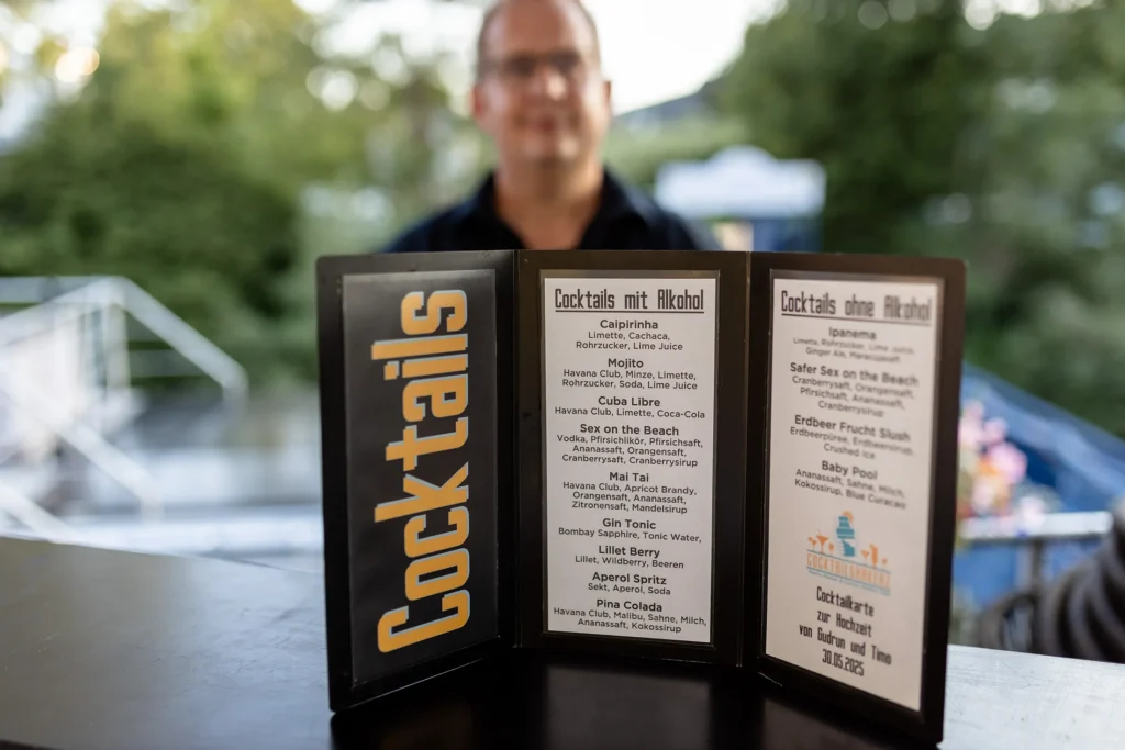 Hochzeitsfotograf Bernkastel Trier - Detailaufnahme der Cocktail-Karte auf der Theke. Im Hintergrund unscharf zu sehen: Marco von den Cocktailshakerz