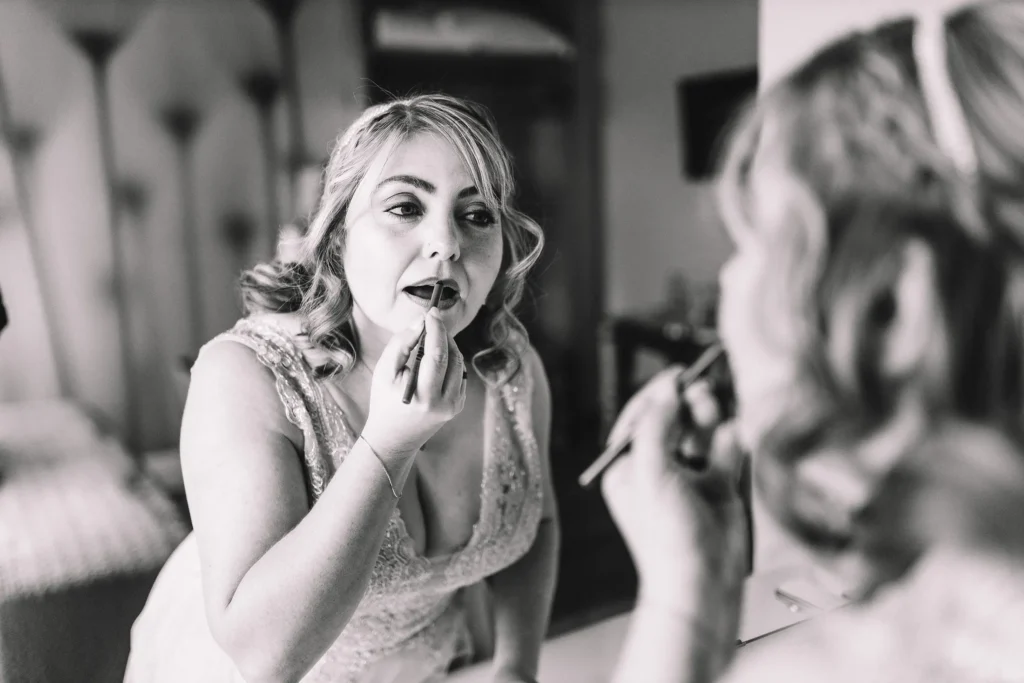 Schwarz-weiss Aufnahme der Braut, wie sie sich vor dem Spiegel den Lippenstift nachzieht beim Getting Ready im Hotelzimmer