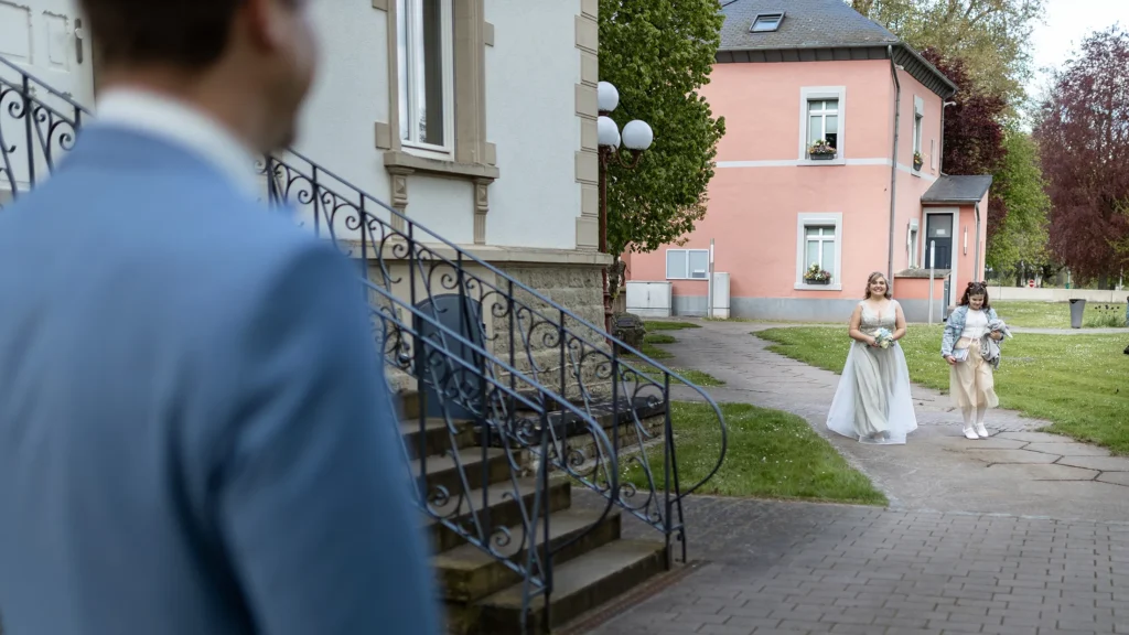 Hochzeitsfotograf Luxemburg - Bräutigam angeschnitten von hinten unscharf zu sehen, während Braut und Tochter für den First Look auf ihn zukommen