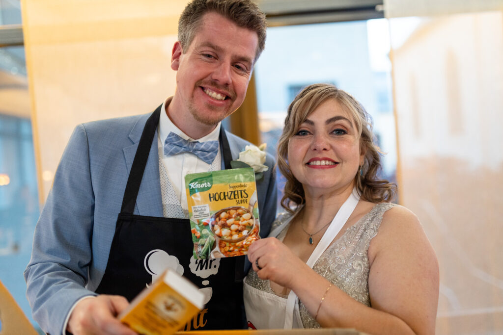 Hochzeitsfotograf Luxemburg - Das Brautpaar hat eine Tüte Hochzeits-Suppe von Knorr geschenkt bekommen und hält diese stolz in die Kamera.