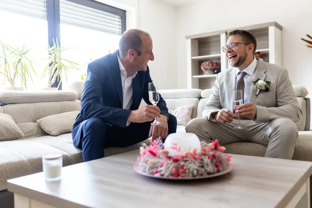 Hochzeitsfotograf Merzig Trier - Der Bräutigam und Trauzeuge geniessen ein Glas Sekt vor der Hochzeit und lachen zusammen herzlich.