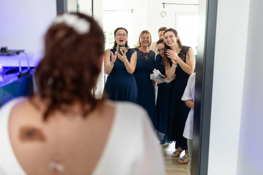 Hochzeitsfotograf Merzig Trier - Man sieht den Rücken der Braut links im Vordergrund unscharf. Rechts im Bild sieht man scharf die Brautjungfern, die gerade Beifall klatschen, als die Braut mit ihrem Hochzeitskleid den raum betritt.