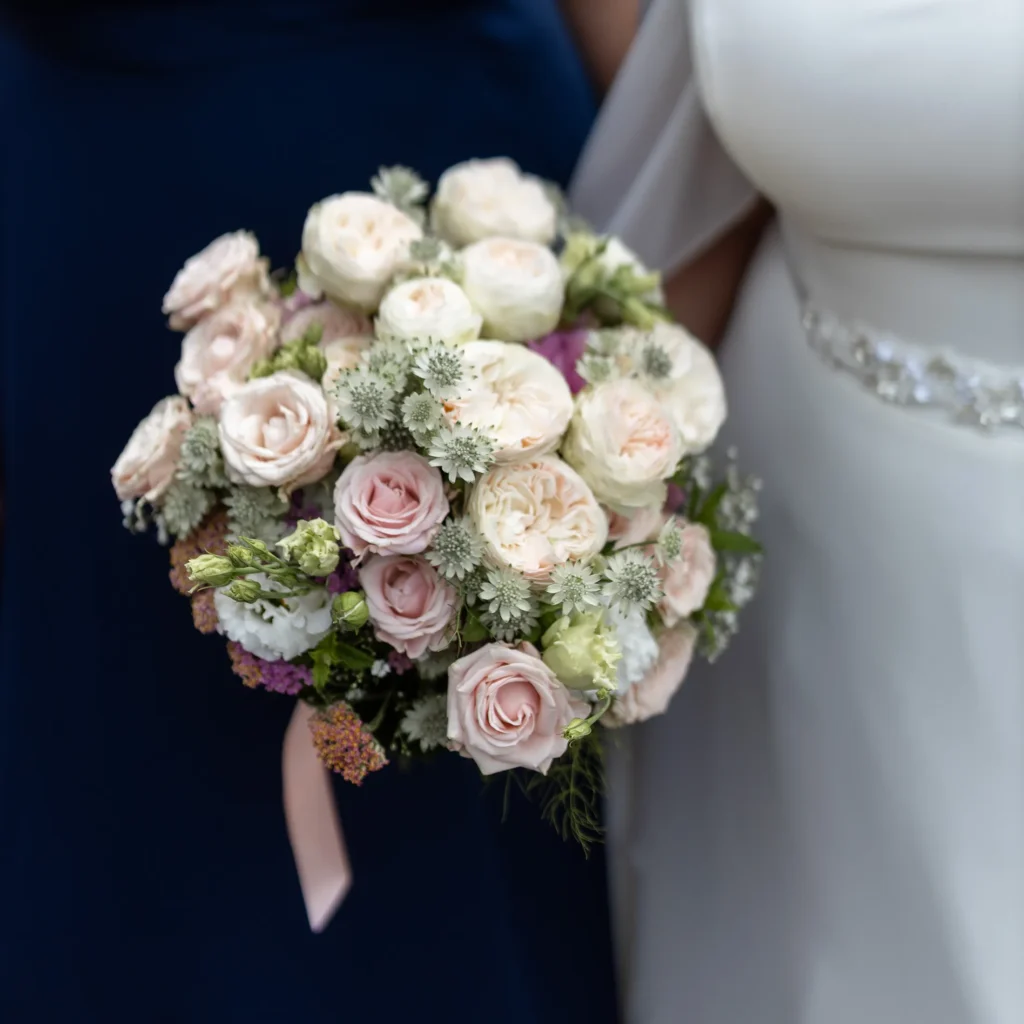Hochzeitsfotograf Merzig Trier - Foto vom Brautstrauss. Im Hintergrund ist das weisse Brautkleid und ein blaues Brautjungfern-Kleid unscharf zu sehen