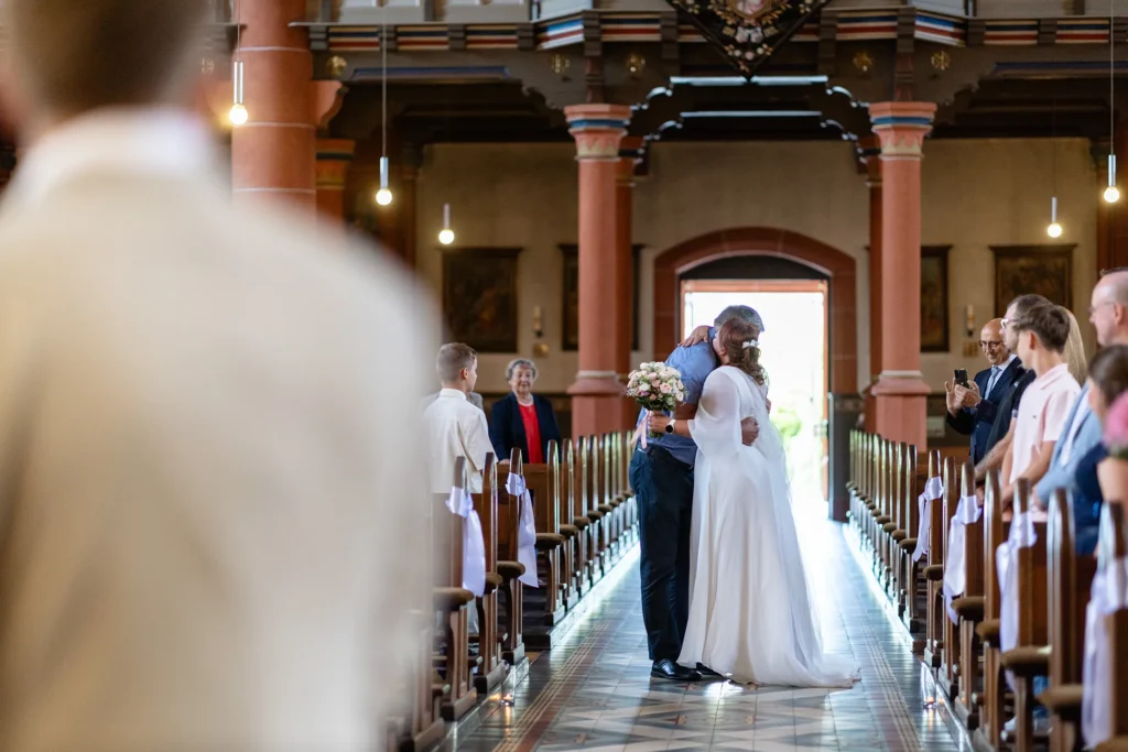 Hochzeitsfotograf Merzig Trier - Die Braut umarmt ihren Vater im Mittelgang der Kirche, kurz bevor er sie an den Sohn übergibt, der die letzten Schritte mit ihr bis zum Altar geht.