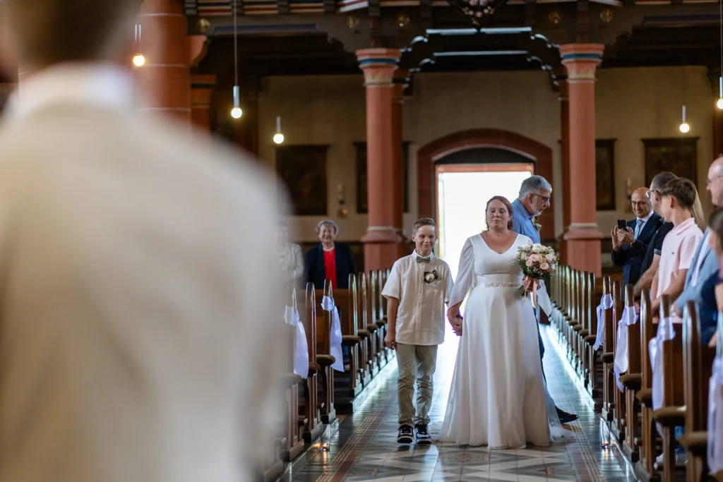 Hochzeitsfotograf Merzig Trier - Die Braut steht mit ihrem Sohn an der Hand im Mittelgang der Kirche und atmet noch einmal tief durch, bevor die Trauung beginnt.