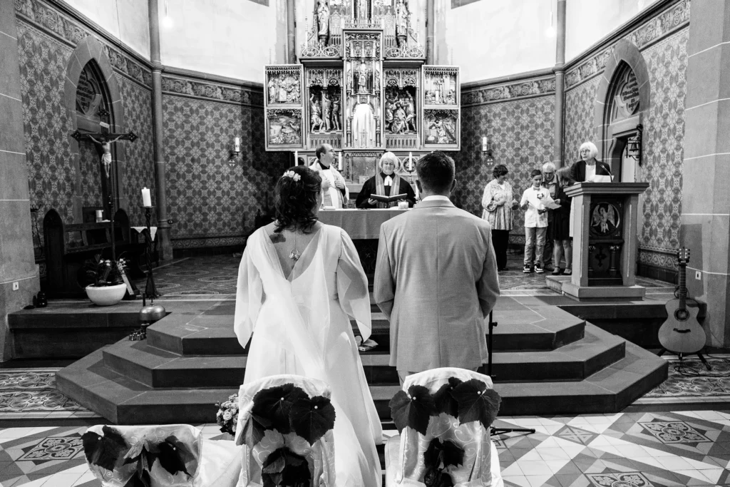 Hochzeitsfotograf Merzig Trier - Brautpaar von hinten in der Kirche während der Zeremonie. Man sieht den Altar.