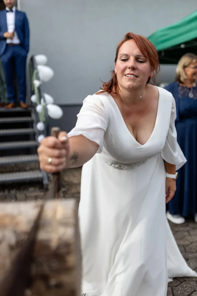 Hochzeitsfotograf Merzig Trier - Die Braut beim traditionellen Baumstamm-Sägen auf der Hochzeit in Merzig