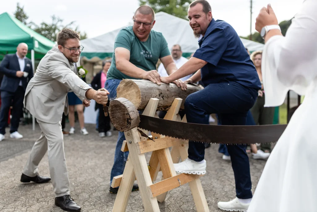 Hochzeitsfotograf Merzig Trier - Der Bräutigam tätigt den letzten Schnitt beim Baumstamm-Sägen. Das abgesägte Teil fällt im Moment herunter