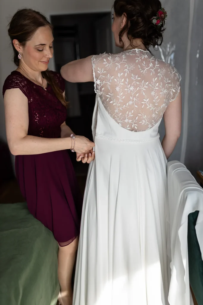 Hochzeitsfotograf Trier Luxemburg - Die Trauzeugin hilft der Braut beim Schliessen des Reissverschlusses des Brautkleids beim Getting Ready.