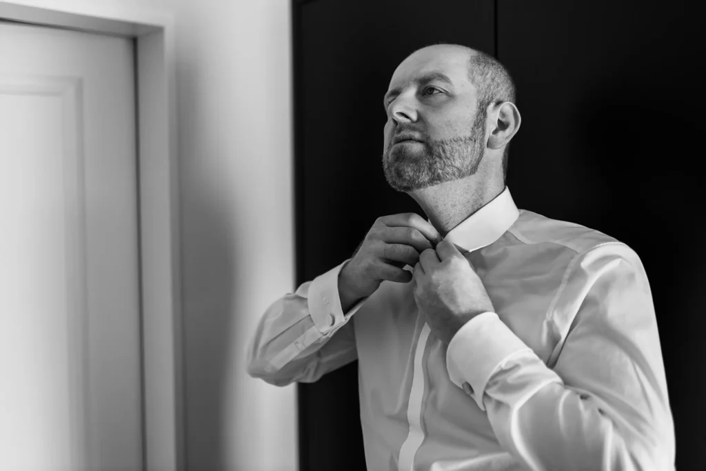 Hochzeitsfotograf Trier Luxemburg - schwarz-weiss Aufnahme des Bräutigams, wie er den obersten Knopf seines Hemds zuknöpft