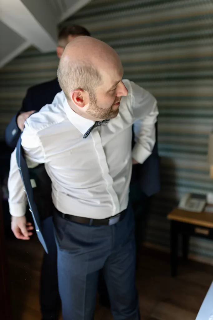 Hochzeitsfotograf Trier Luxemburg - Der Trauzeuge steht hinter dem Bräutigam und hilft ihm dabei, die Weste anzuziehen.