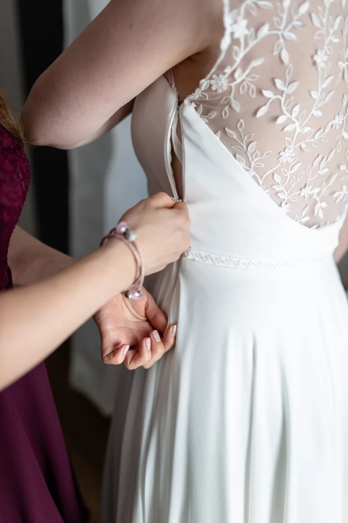 Hochzeitsfotograf Trier Luxemburg - Nahaufnahme, wie die Trauzeugin den Reissverschluss des Brautkleides schliesst.