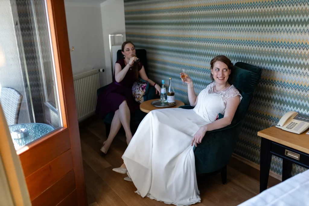 Hochzeitsfotograf Trier Luxemburg - Braut und Trauzeugin geniessen noch schnell ein Glas Wein im Hotelzimmer, bevor die Trauung beginnt.