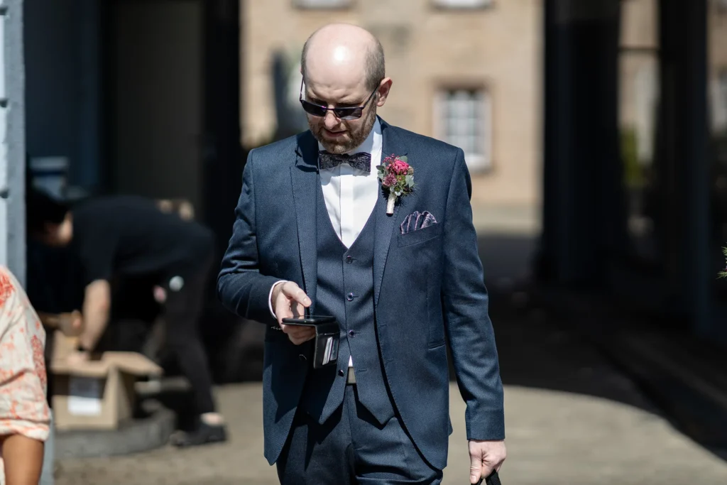 Hochzeitsfotograf Trier Luxemburg - Der Bräutigam steht vor dem Turm Jerusalem in Trier und checkt noch schnell das Handy, kurz bevor die Braut kommt.