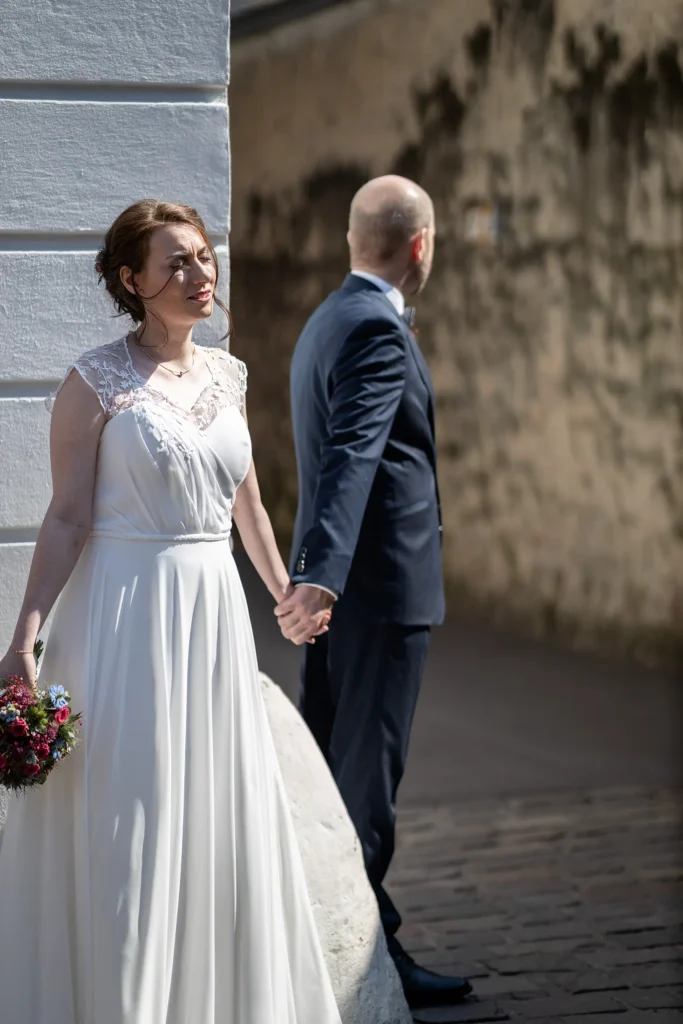 Hochzeitsfotograf Trier Luxemburg - Hochkant Variante des Bilds, wo Braut und Bräutigam Hänchen haltend an einer Ecke stehen, ohne sich sehen zu können.