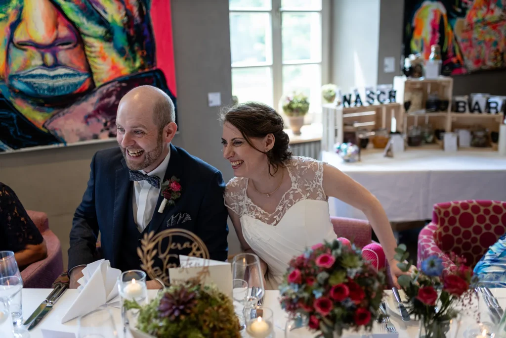 Hochzeitsfotograf Trier Luxemburg - Brautpaar sitzt am Tisch und beide lachen herzlich