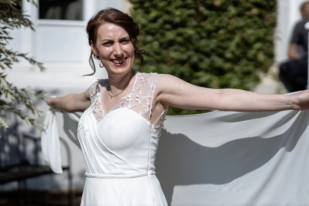 Hochzeitsfotograf Trier Luxemburg - Die Braut breitet beide Arme aus und fächert ihren Schleier im Nells Park im Sonnenschein.