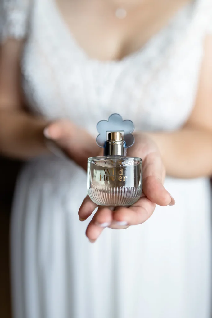 Hochzeitsfotograf Trier Luxemburg - Nahaufnahme des Parfums der Braut. Im Hintergrund ist in der Unschärfe das weisse Brautkleid zu sehen.