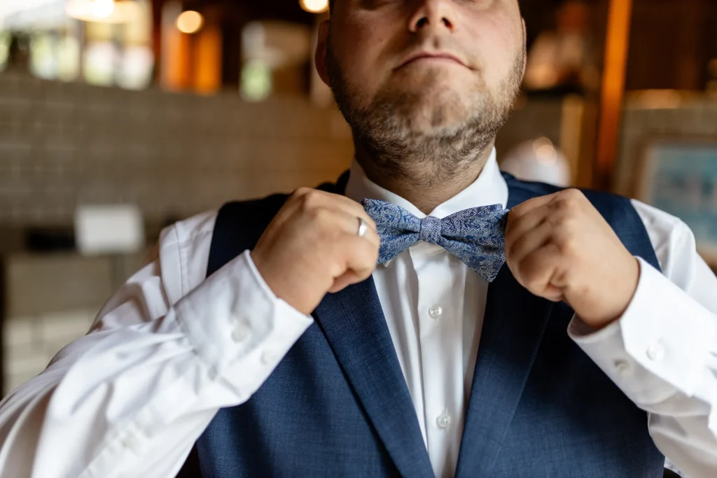 Hochzeitsfotograf Trier Luxemburg - Detailaufnahme mit ungewöhnlicher Perspektive: Der Bräutigam richtet sich die Fliege. Sein Kopf ist oberhalb der Nase abgeschnitten und nicht zu sehen.