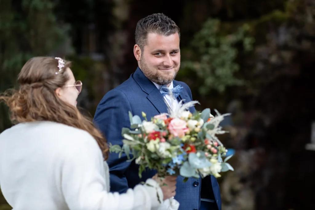 Hochzeitsfotograf Trier Luxemburg - Der Bräutigam dreht sich gerade für den First Look um und sieht aus den Augenwinkeln seine Frau zum ersten Mal im Hochzeitskleid. Die Braut ist auf dem Foto nur von hinten zu sehen.