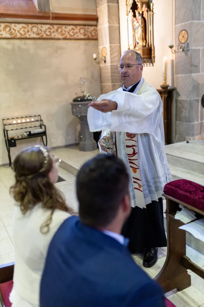 Hochzeitsfotograf Trier Luxemburg - Der Pfarrer streut während der Trauungs-Zeremonie Konfetti auf das Brautpaar, weil die beiden sich während des Faschings kennen gelernt haben.