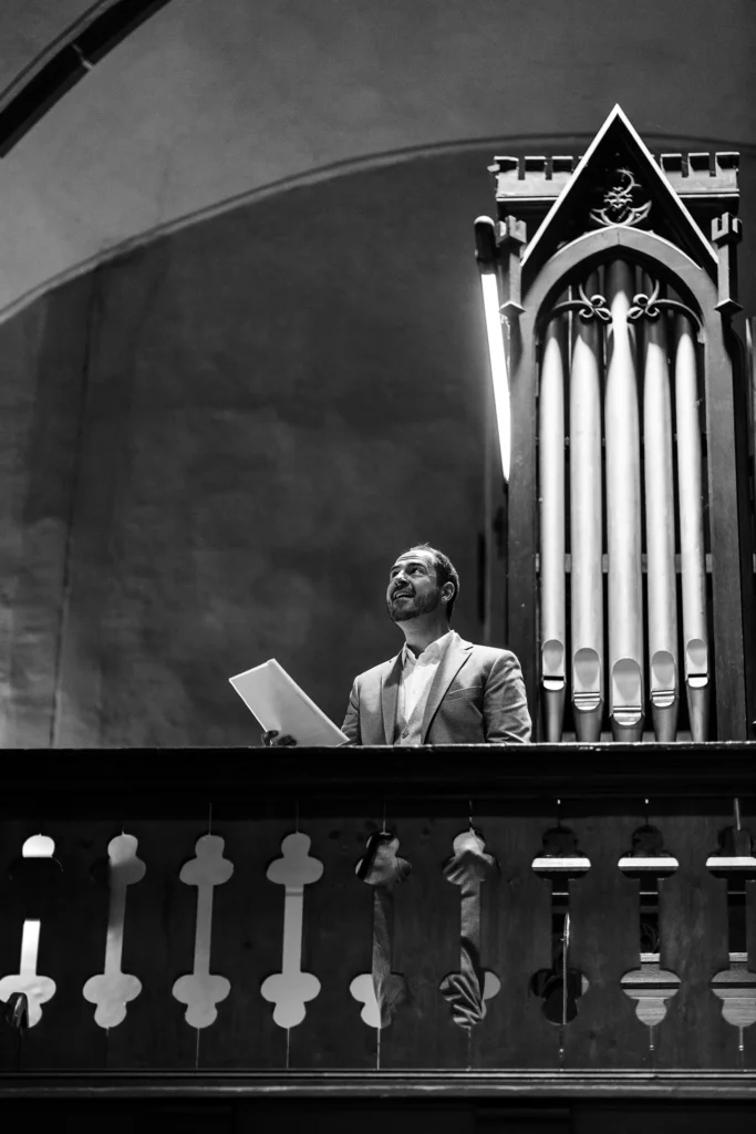 Hochzeitsfotograf Trier Luxemburg - Der Sänger, der während der Hochzeit singt steht neben der Orgel oben im Kirchenschiff und schaut verträumt nach oben während er singt. Schwarz-weiss Aufnahme