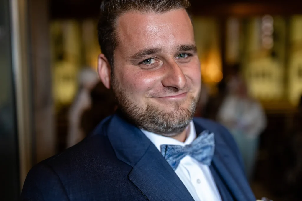 Hochzeitsfotograf Trier Luxemburg - Portraitaufnahme des grinsenden Bräutigams während der Gratulation von den Hochzeits-Gästen.