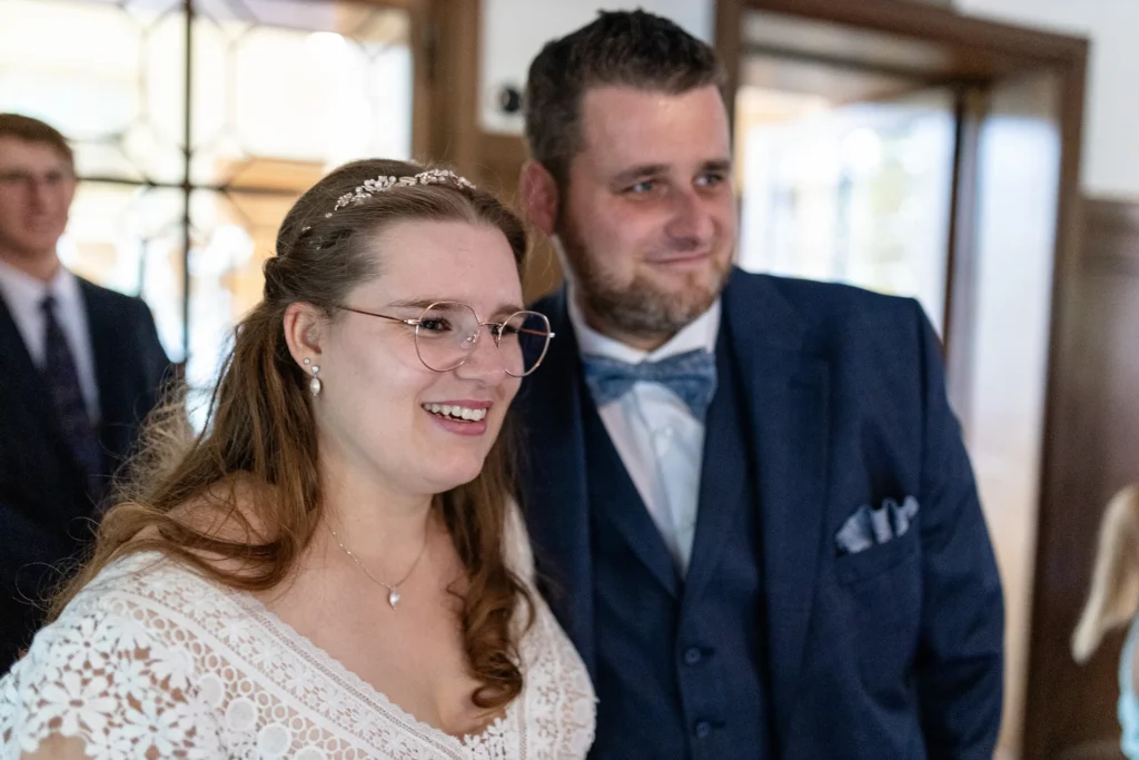 Hochzeitsfotograf Trier Luxemburg - Die Braut lächelt, während sie sich den für sie einstudierten Tanz der Gäste anschaut. Im Hintergrund in der Unschärfe ist der Bräutigam zu sehen.