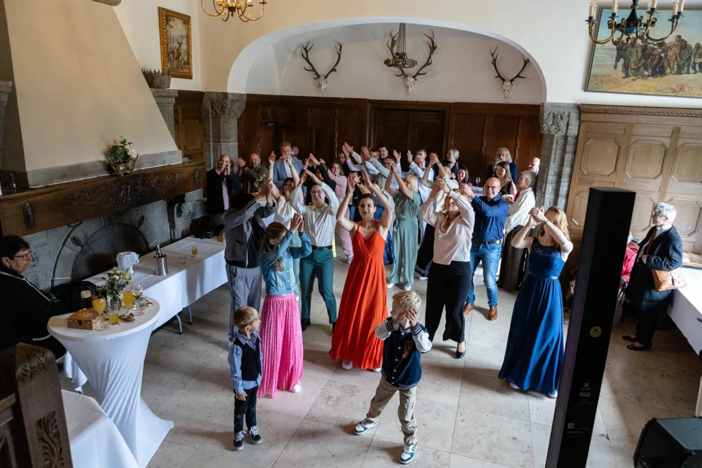 Hochzeitsfotograf Trier Luxemburg - Tanzsaal des Schlosses: Hier tanzen viele Gäste einen abgestimmten Tanz und halten im Moment ihre Hände synchron hoch.