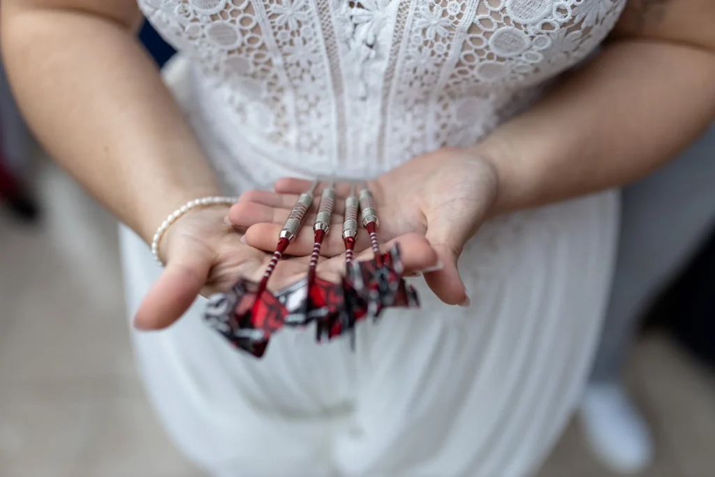 Hochzeitsfotograf Trier Luxemburg - Nahaufnahme der Dart-Pfeile, die die Braut in den Händen hält. Im Hintergrund ist unscharf das Brautkleid zu sehen.