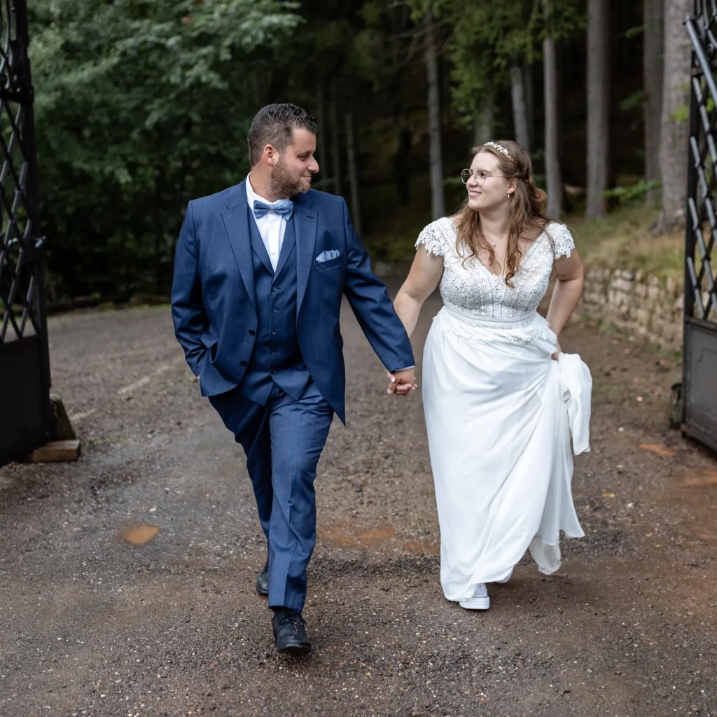 Hochzeitsfotograf Trier Luxemburg - Brautpaar-Foto-Shooting: Das Brautpaar sieht sich an und kommt auf den Fotografen zu, während sie durch ein schmiedeeisernes Tor spazieren.