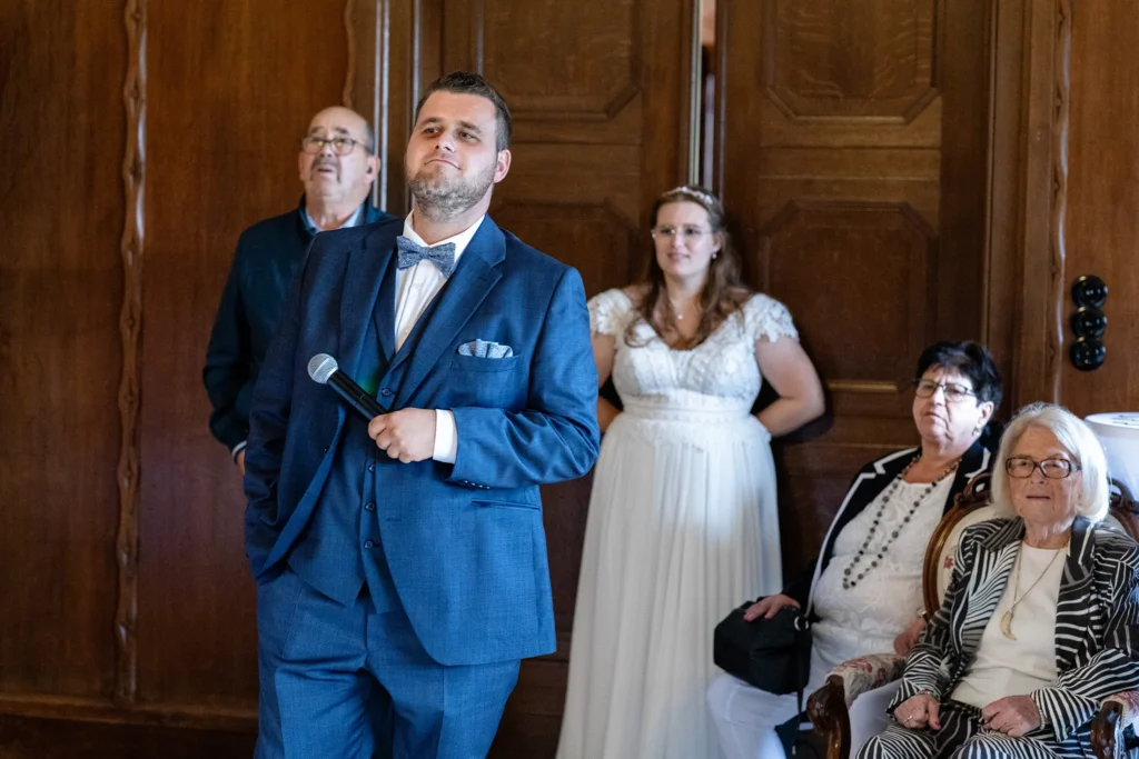 Hochzeitsfotograf Trier Luxemburg - Der Bräutigam hat gerade das Essen eröffnet und hält noch das Mikrofon in der Hand und visiert einen bestimmten Gast lächelnd an.